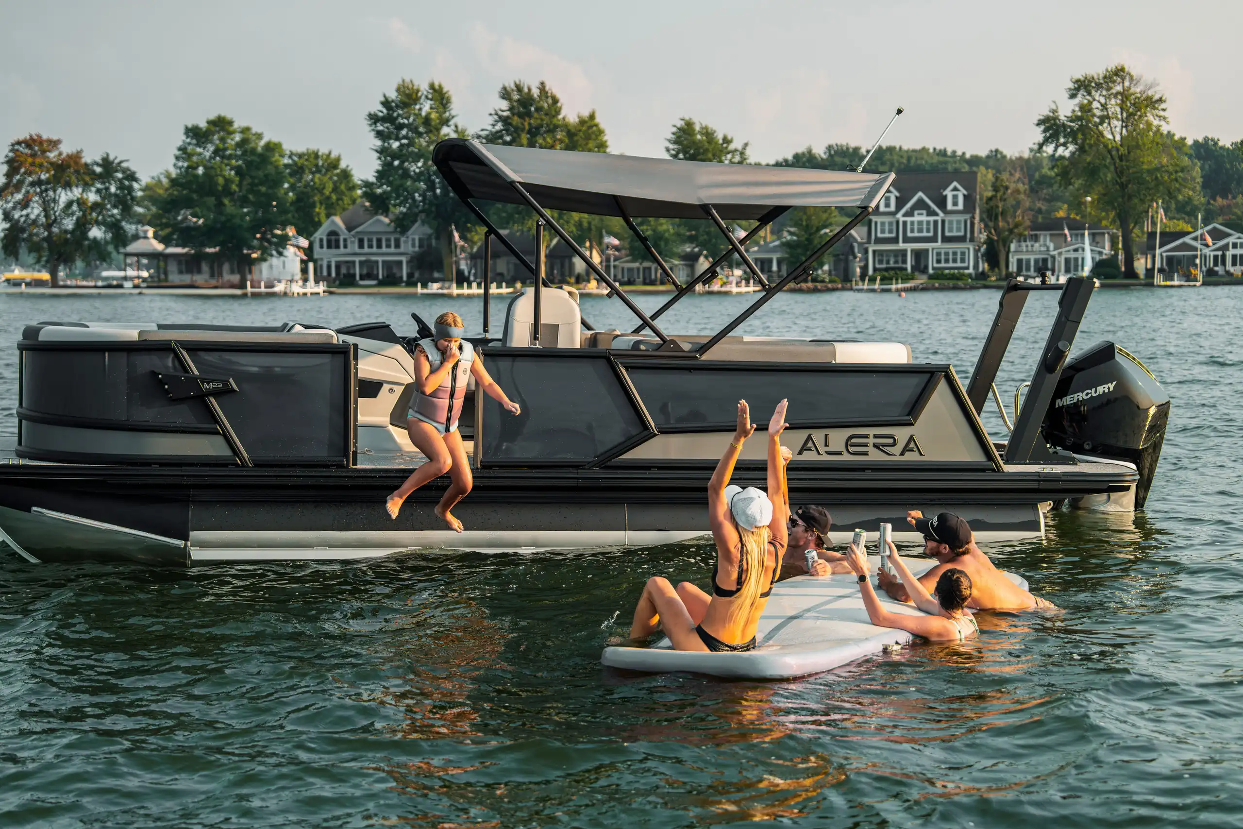 Friends jumping off an Alera pontoon boat into the lake on a sunny day.